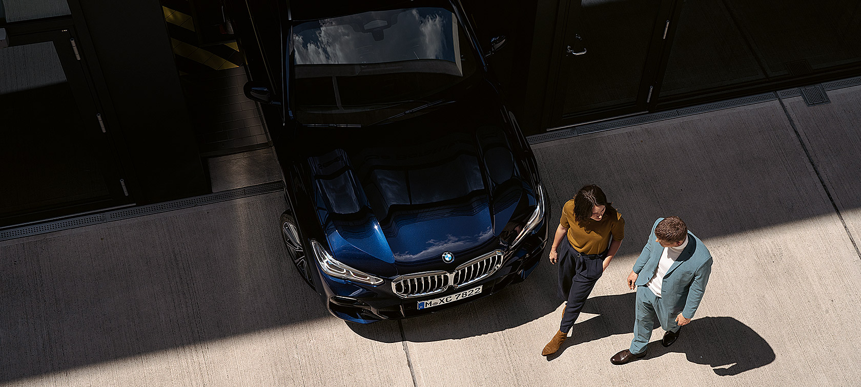 Vrouw en man lopen langs voorzijde BMW bovenaanzicht